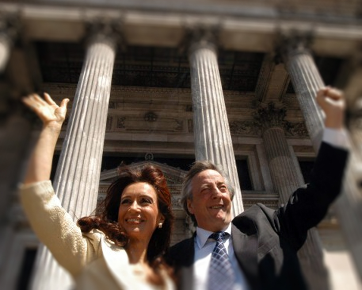 Cristina Fernández y Néstor Kirchner sonrientes, saludando con los brazos en alto